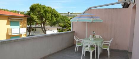 A balcony with a table and chairs, an umbrella, and a view of neighboring buildings.