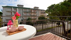 A balcony with a table set for tea, a vase with flowers, and a view of a residential area with buildings and trees. - Cozy flat 350mt from the beach (Bibione)
