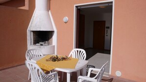 Eine Terrasse im Freien mit einem weißen Tisch und Stühlen, einem Pizzaofen und einer gelben Tischdecke.