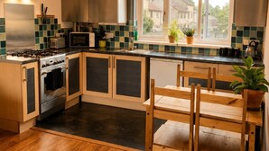 A modern kitchen with a central island, stainless steel appliances, and a window with a view of houses. - Family Friendly Coach House - Parking - Sleeps 4 (Weston-super-Mare)