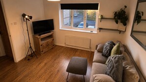 A living room with a television, wooden floor, and a window with blinds. - Family Friendly Coach House - Parking - Sleeps 4 (Weston-super-Mare)