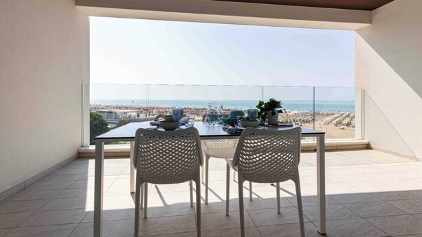 Un balcón con mesa y sillas, con vista a la playa y al paisaje urbano.