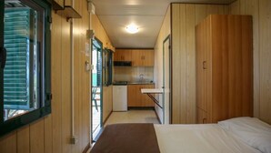 A compact room with wooden walls, a kitchenette, a bed, and a window with blinds.