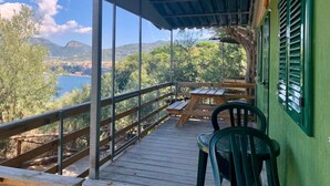 A covered outdoor deck with a wooden table and chairs, overlooking a scenic landscape with trees and a body of water.