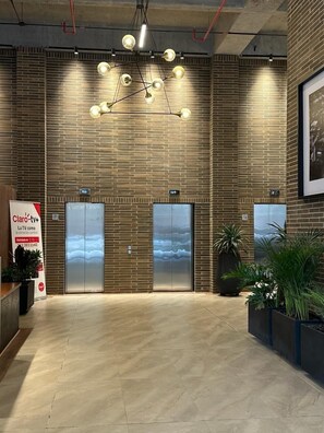 Eine Lobby mit modernem Design, ein Backsteinwand, eine Kronleuchter, zwei Aufzüge und Kübelpflanzen.