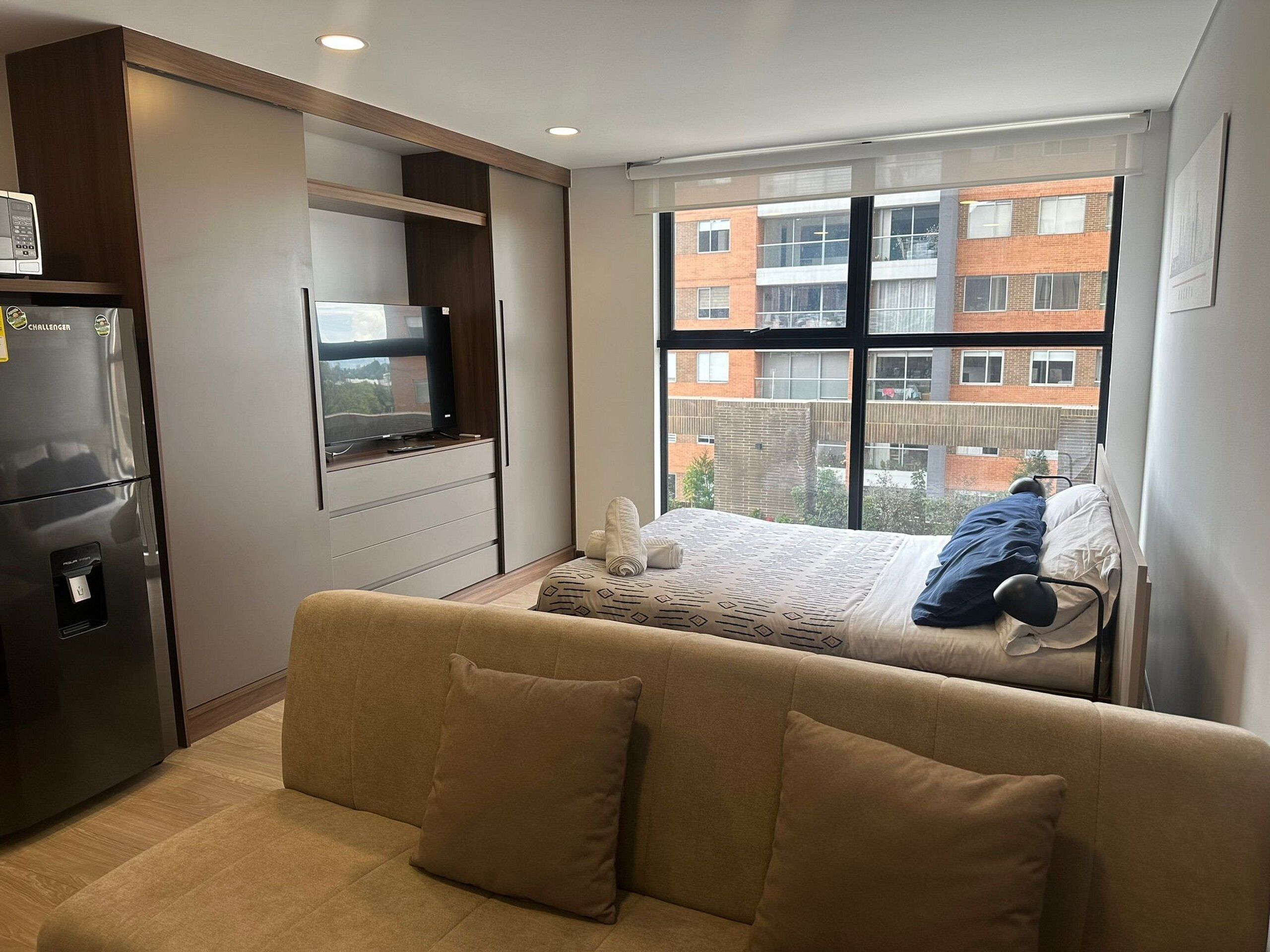 Ein kompakter Wohnraum mit Küchenzeile, einem Bett, einer Couch und einem großen Fenster mit Blick auf die Stadt.