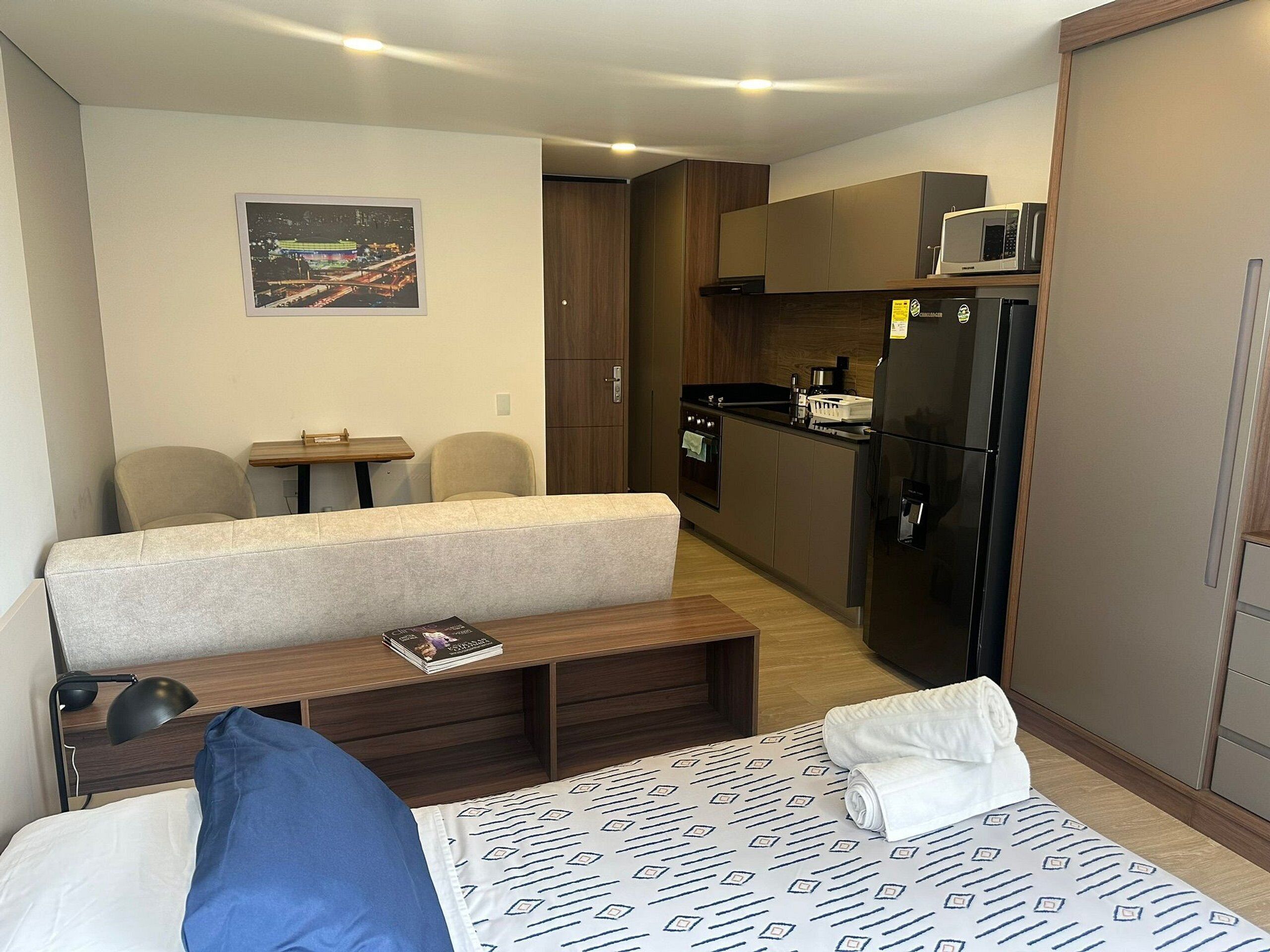 Habitación de hotel compacta con cama, un pequeño escritorio, kitchenette y zona de estar.
