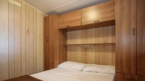 A bedroom with a wooden bunk bed and a single bed, wooden wardrobe with multiple compartments, and a built-in shelf above the single bed.