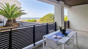 Un balcon avec une table et des chaises, un palmier, et une vue sur la plage et l’océan.