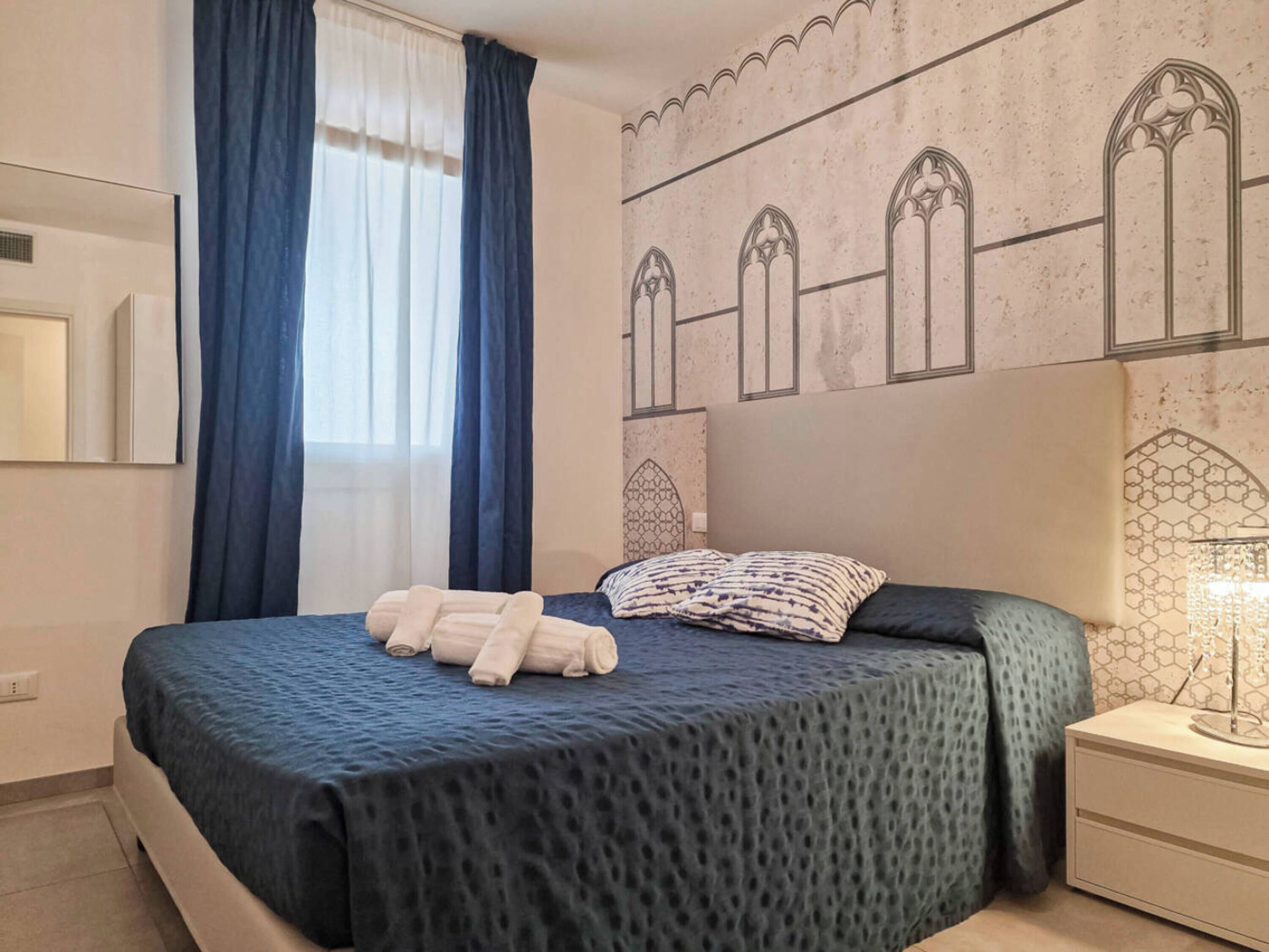 A hotel room with a bed, a nightstand, a lamp, and a window with curtains.