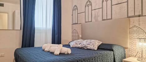 A hotel room with a bed, a nightstand, a lamp, and a window with curtains.