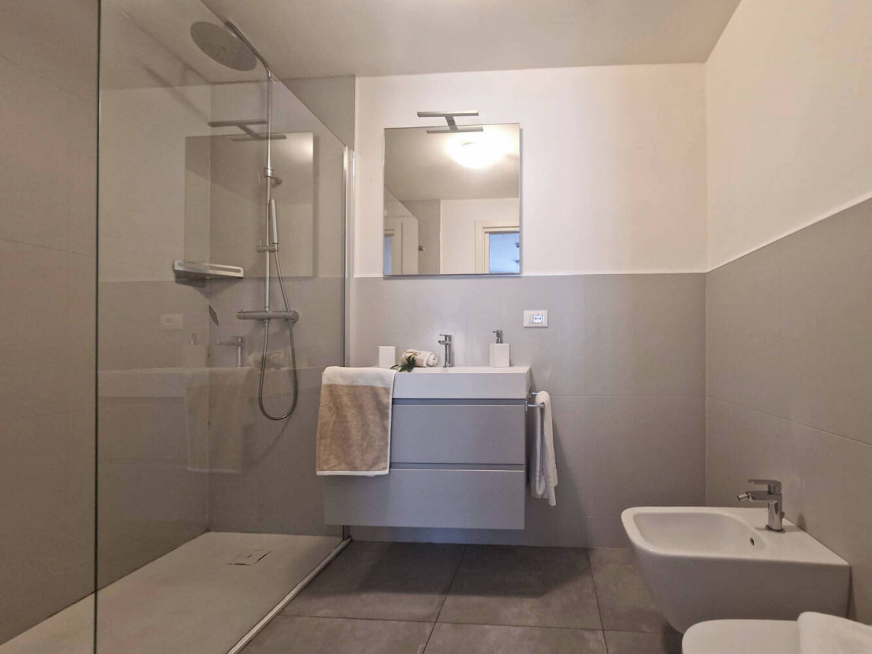 Un baño moderno con ducha de vidrio, lavamanos con espejo y un área de inodoro separada.