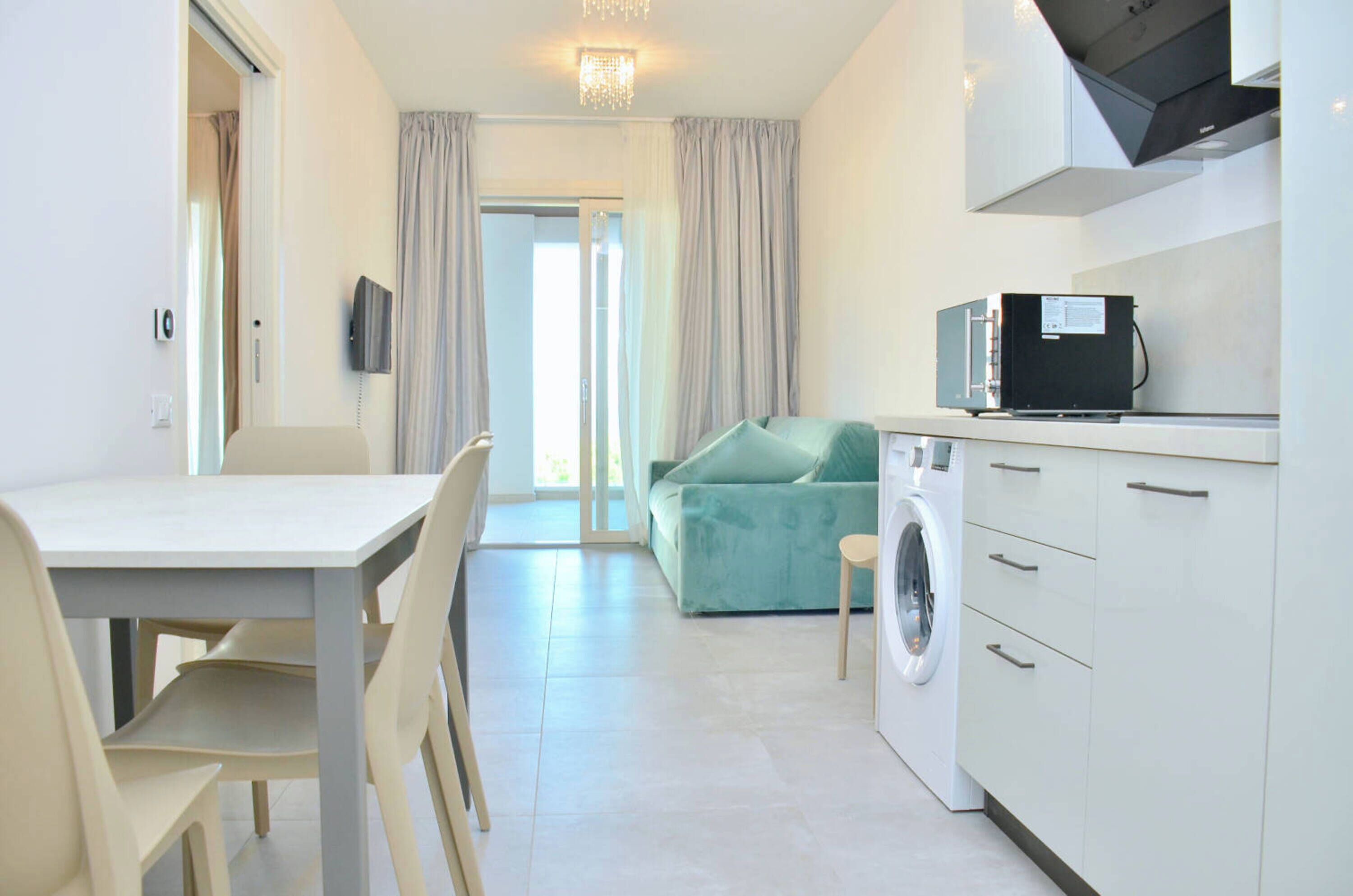 A compact hotel room with a dining area, a sofa, a washing machine, and a kitchenette.