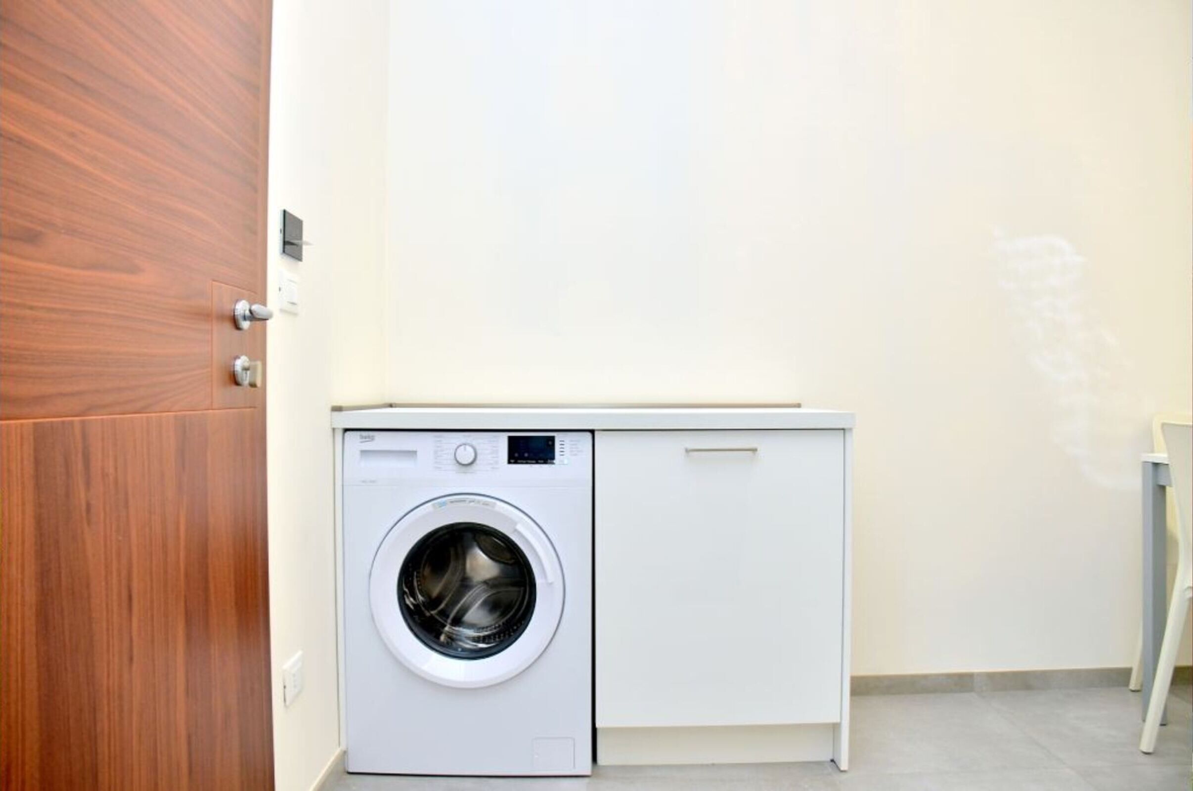 Un lavadero pequeño con lavadora, una puerta de madera y un armario blanco.