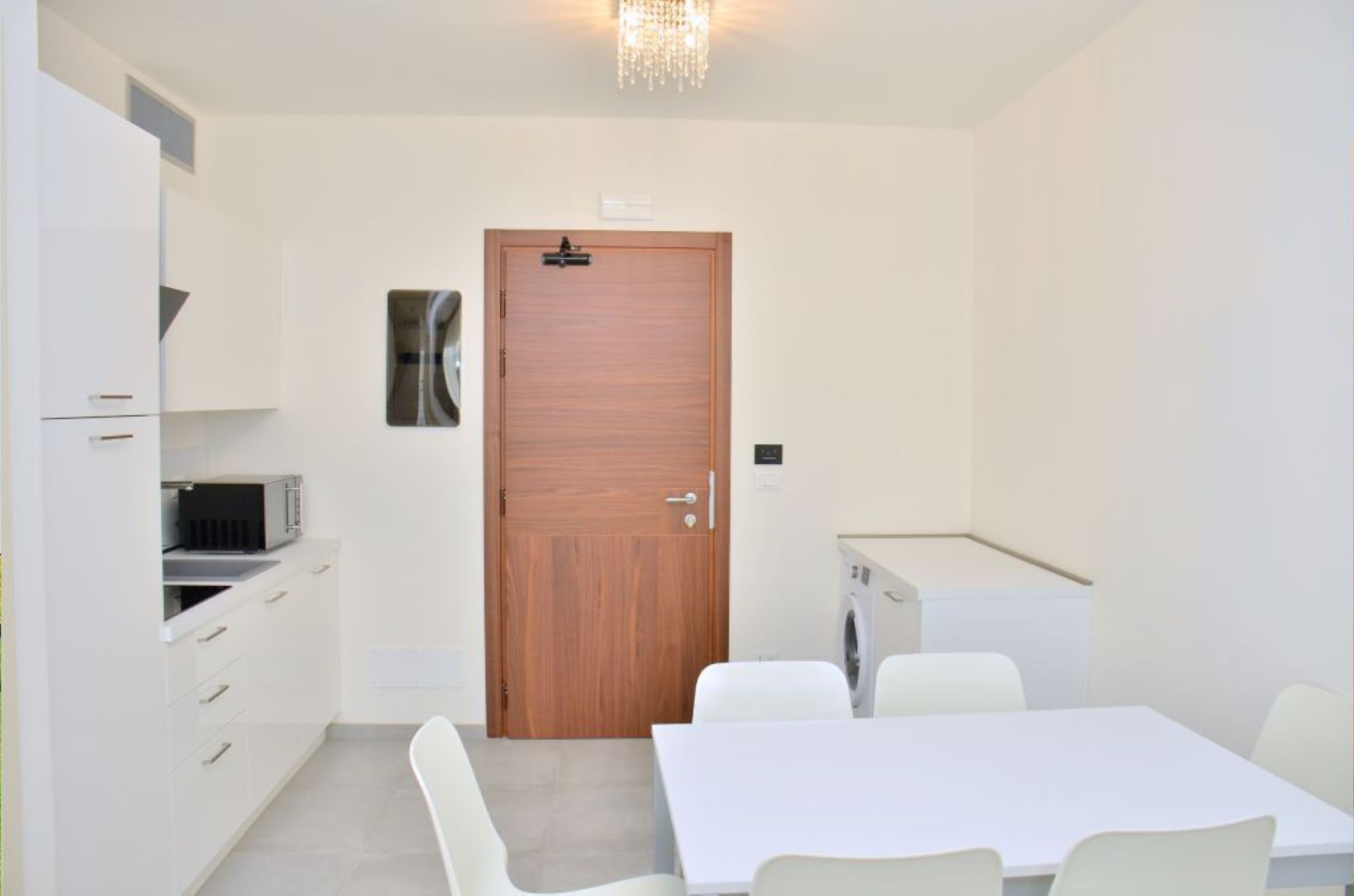 Een compacte, moderne keuken met witte kasten, een houten deur en een kleine eethoek met een tafel en stoelen.