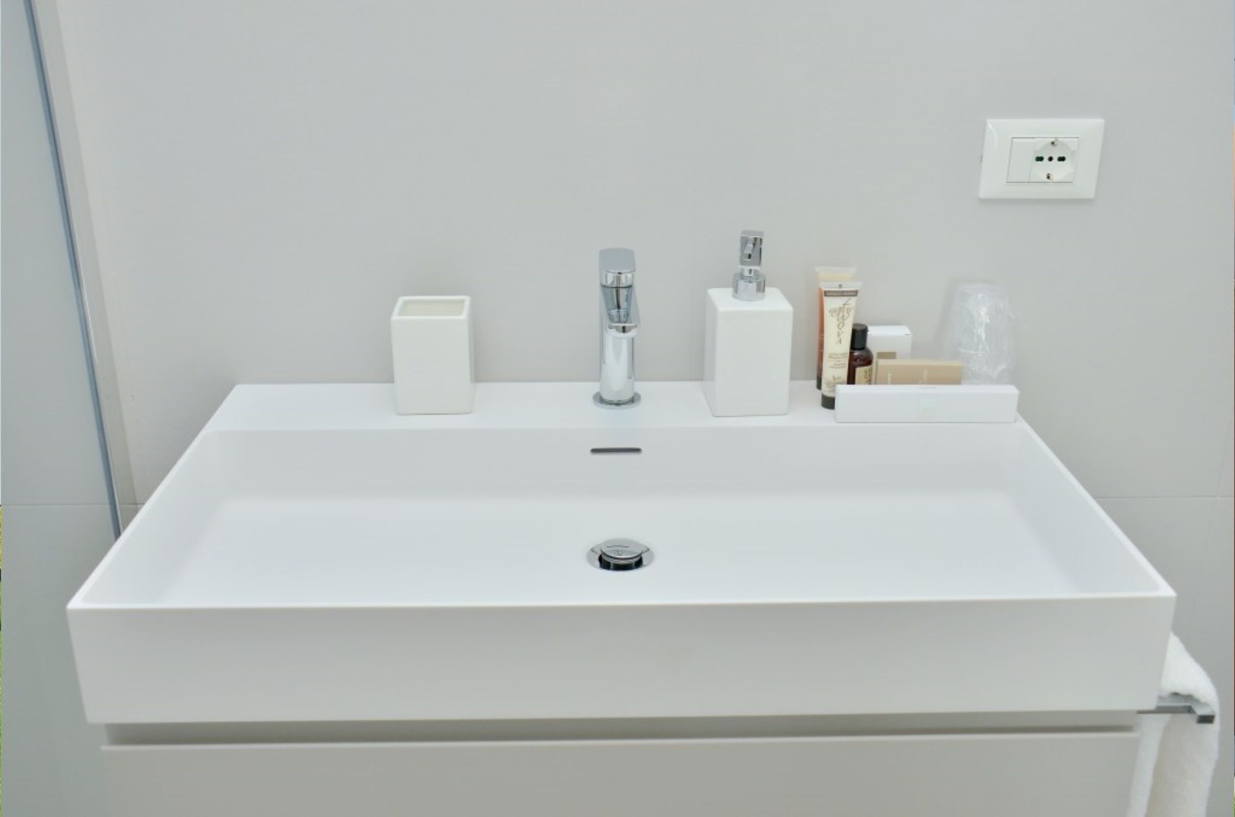 Un lavabo blanc dans une salle de bain, doté d’un robinet moderne, d’un distributeur de savon et d’un petit flacon de savon liquide posé sur le comptoir.