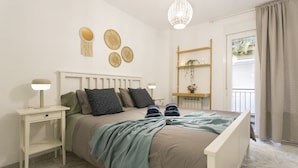 Camera da letto con un letto, comodini, una lampada a sospensione, una finestra con tende e un piccolo ripiano con una pianta.