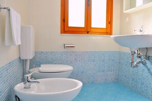 Ein Badezimmer mit Toilette, Bidet und Waschbecken, mit blauen und weißen Fliesen, und einem Fenster über dem Waschbecken.