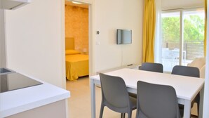 A compact hotel room with a kitchenette, a bed with yellow bedding, a TV mounted on the wall, and a balcony with yellow curtains. - Beautiful apartment lighted by the sun in Bibione (Bibione)