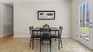 Zona pranzo con tavolo e sedie, un quadro appeso al muro e una porta che dà all'esterno.