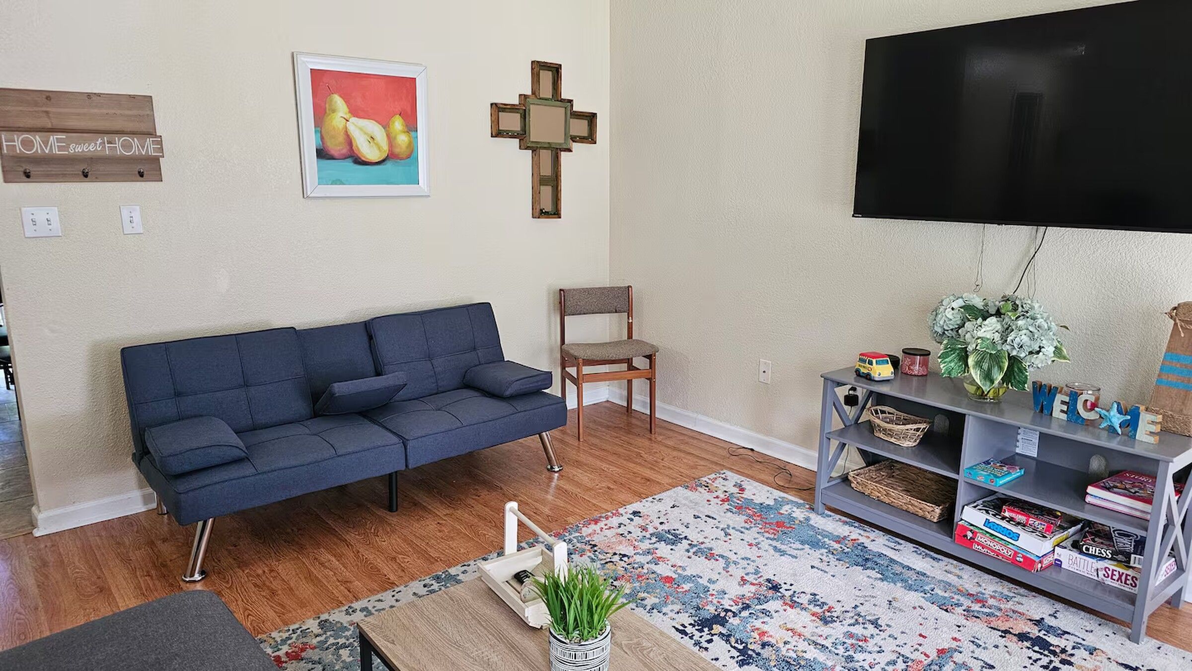 A living room with a blue sofa, a wooden chair, a TV, a bookshelf, and a small table with a plant.