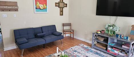 A living room with a blue sofa, a wooden chair, a TV, a bookshelf, and a small table with a plant.
