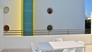 A white table with four chairs outside a building with a white facade, featuring circular windows and a vertical blue stripe. - Coastal studio seaside calm with balcony (Bibione)