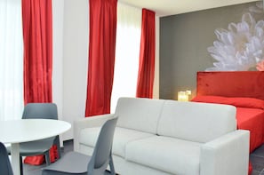 A hotel room with a white sofa, a small round table, and red curtains.