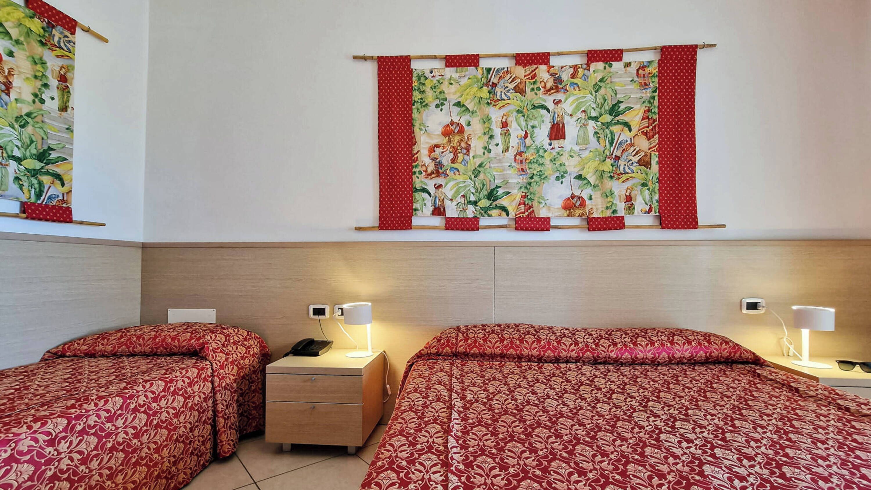 Ein Hotelzimmer mit zwei Betten, einem Nachttisch, Nachttischlampen und einer Wandteppich.