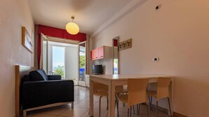 Un espacio habitable pequeño con un sofá, una mesa de comedor con sillas, un televisor y una ventana con marco rojo.