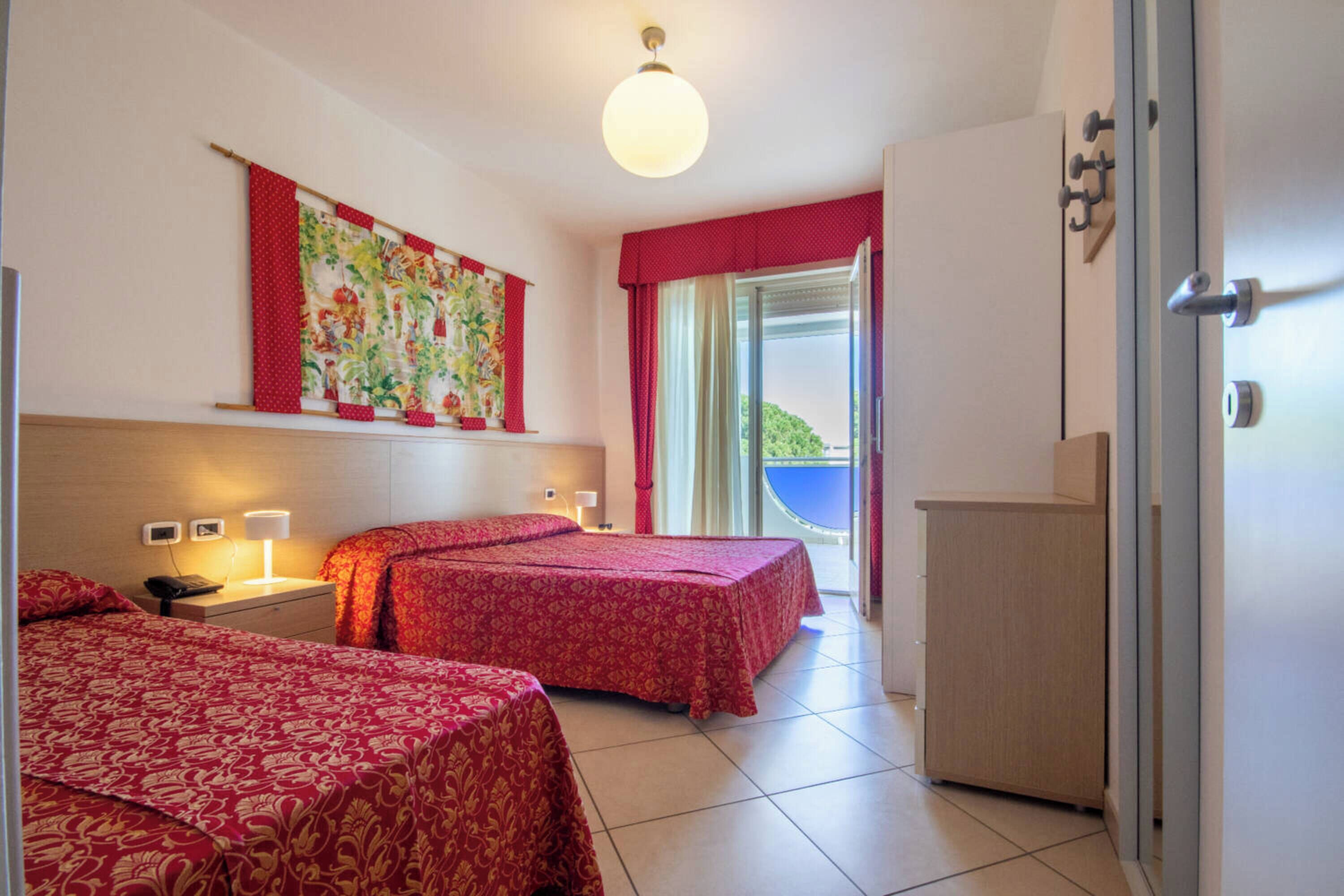 A hotel room with two beds, a large window with a view, a wardrobe, and a wall-mounted artwork.