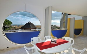 Una habitación con una mesa redonda y sillas, un mantel rojo y vistas a una playa con una estructura de techo de paja.