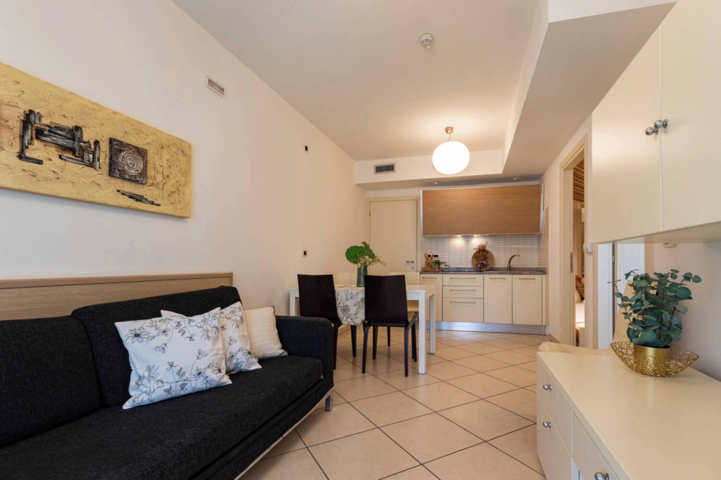 Ein modernes Wohnzimmer mit Sofa, Esstisch, Stühlen und einer Küchenzeile im Hintergrund.