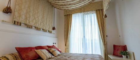 Un dormitorio con cama, cortinas, mesita de noche y lámpara colgante.