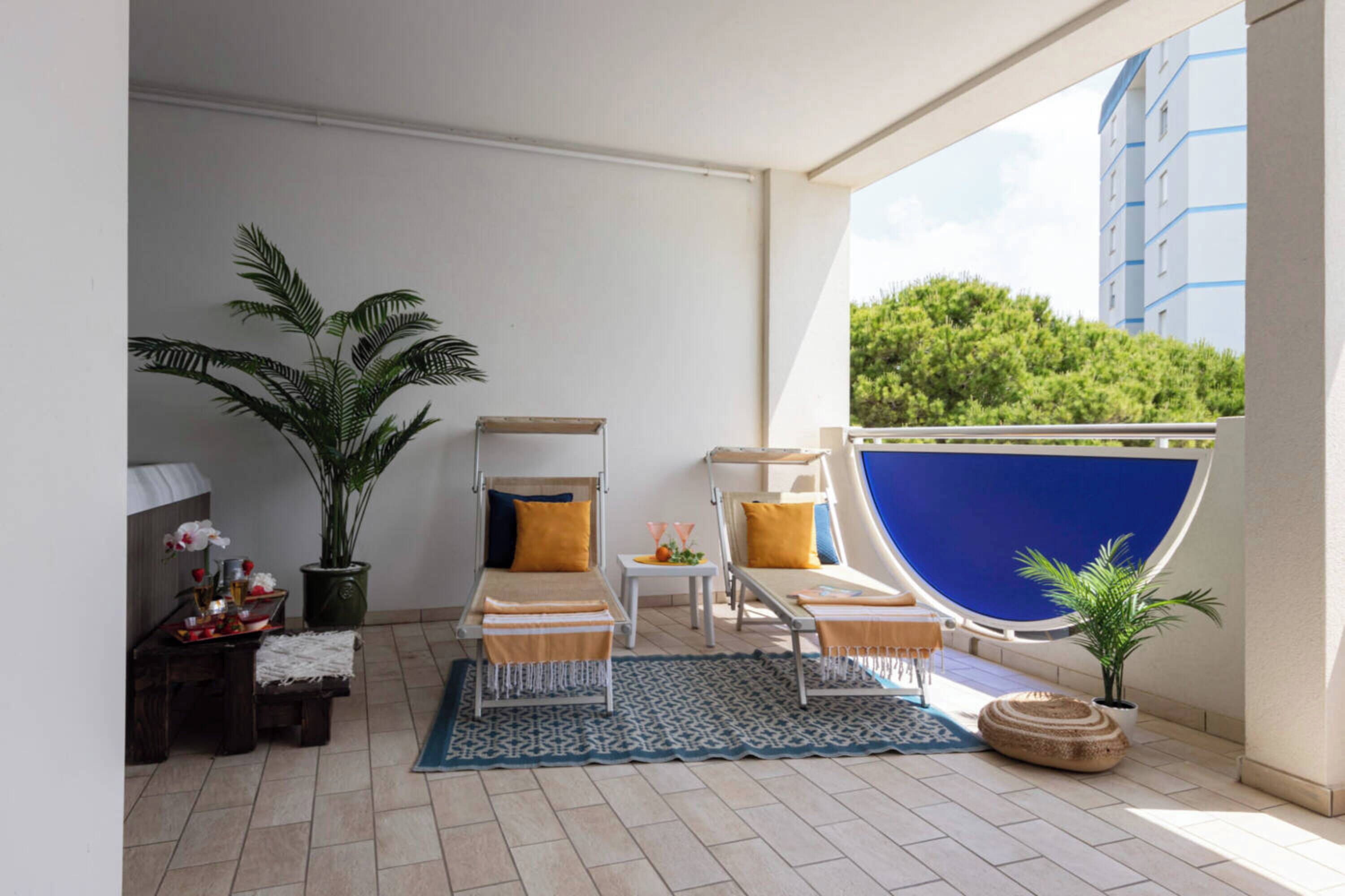 Un balcon avec un espace salon, une petite table, une plante en pot et une vue sur un immeuble et de la verdure.