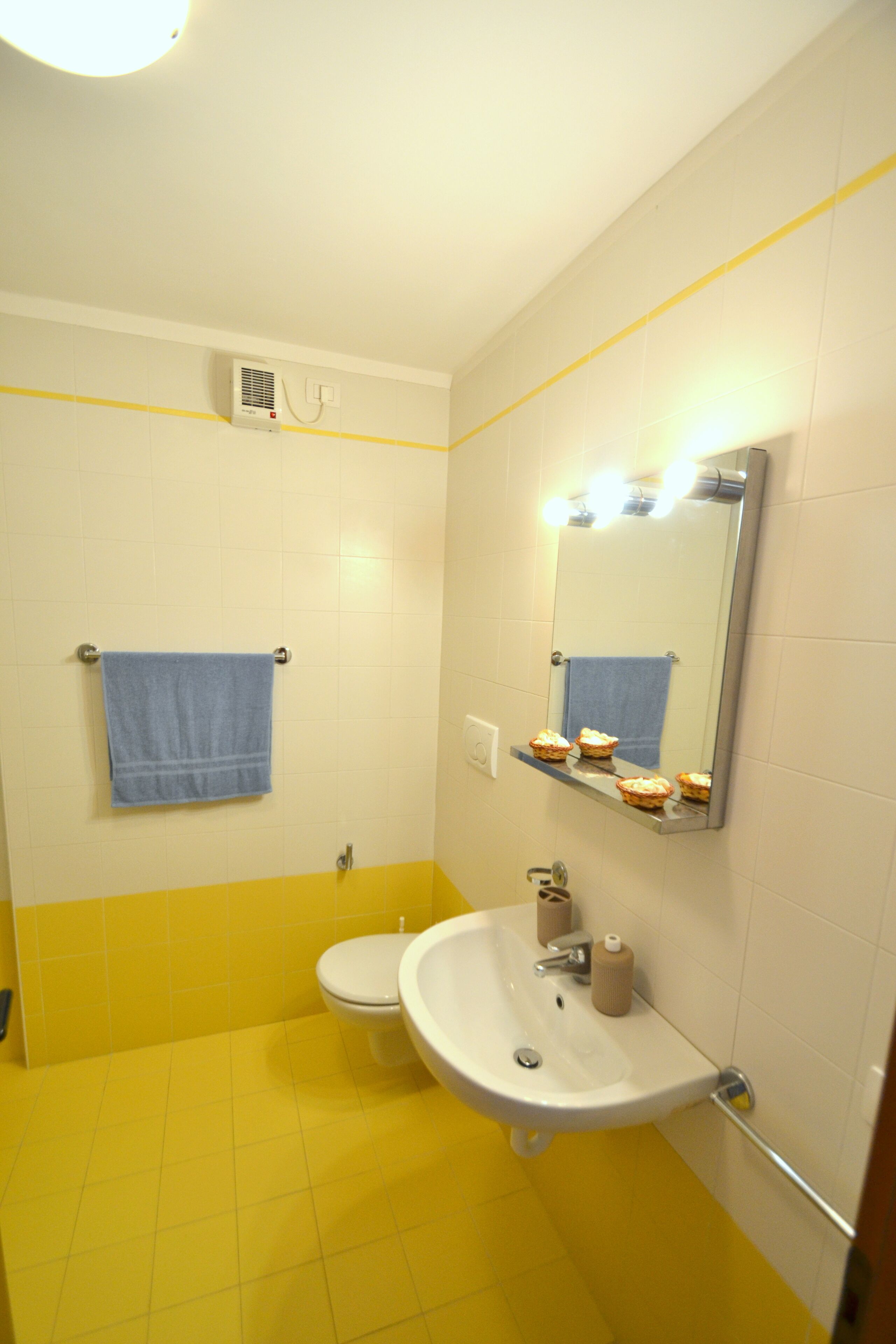 A bathroom with a yellow and white color scheme, a sink, a toilet, a mirror, and a towel rack.