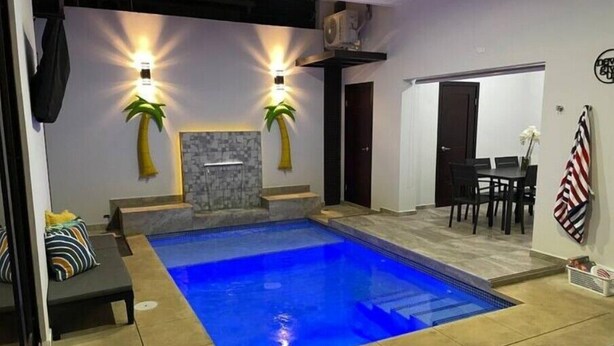 Una piscina interior moderna con pared de piedra y dos adornos de palmera.