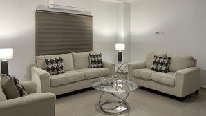 Una sala de estar moderna con dos sofás, una mesa de centro de vidrio, ventilador de techo y aire acondicionado.