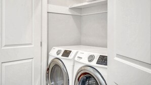 Une buanderie avec deux machines à laver à chargement frontal blanches et une étagère blanche au-dessus.