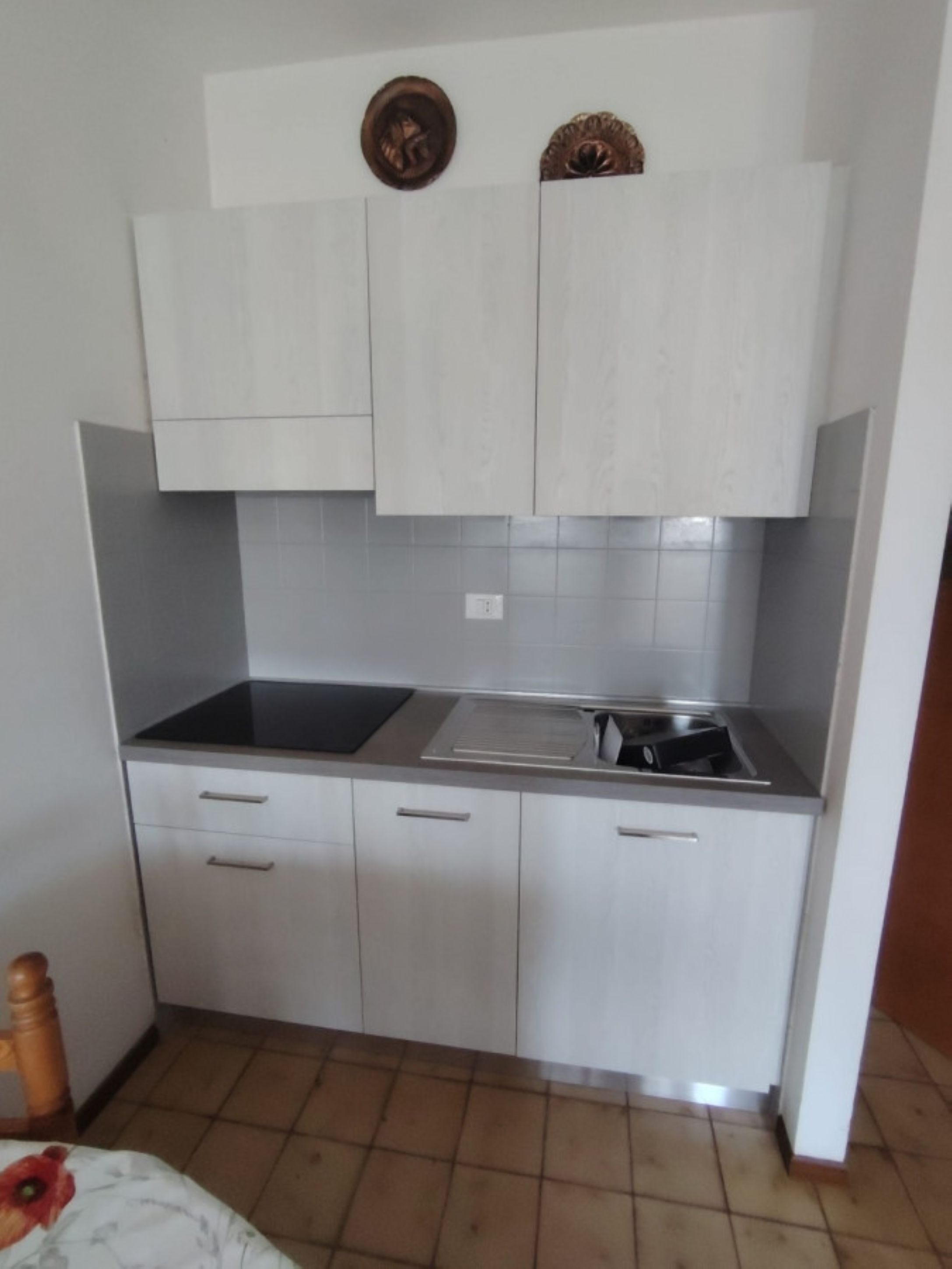 Een kleine keuken met witte kastjes, een zwarte kookplaat en een betegelde achterwand.