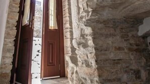 A stone interior with a wooden door and a view of the outside. - Platsa's House (Naxos)