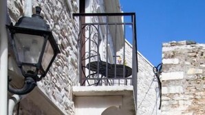 A narrow stone pathway flanked by buildings with stone walls and wooden doors, leading to a higher building with a balcony. - Platsa's House (Naxos)