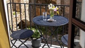 A balcony with a round table, two chairs, a potted plant, and a vase with flowers. - Platsa's House (Naxos)