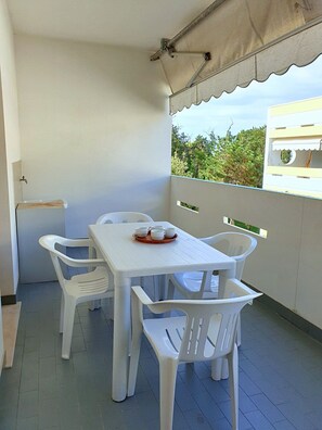 Ein Balkon mit einem weißen Tisch und Stühlen, einem kleinen Spülbecken und Blick auf Grünflächen.