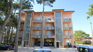 Un immeuble à plusieurs étages doté de balcons, une enseigne indiquant « Al Toschetto », et des voitures garées devant.