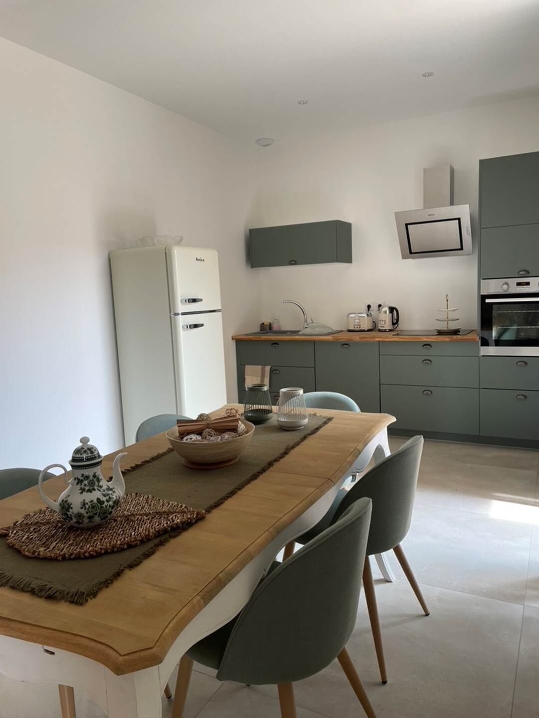 A modern kitchen with a built-in oven, microwave, and sink. There is a dining table with chairs and a decorative teapot.