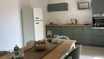 A modern kitchen with a built-in oven, microwave, and sink. There is a dining table with chairs and a decorative teapot.