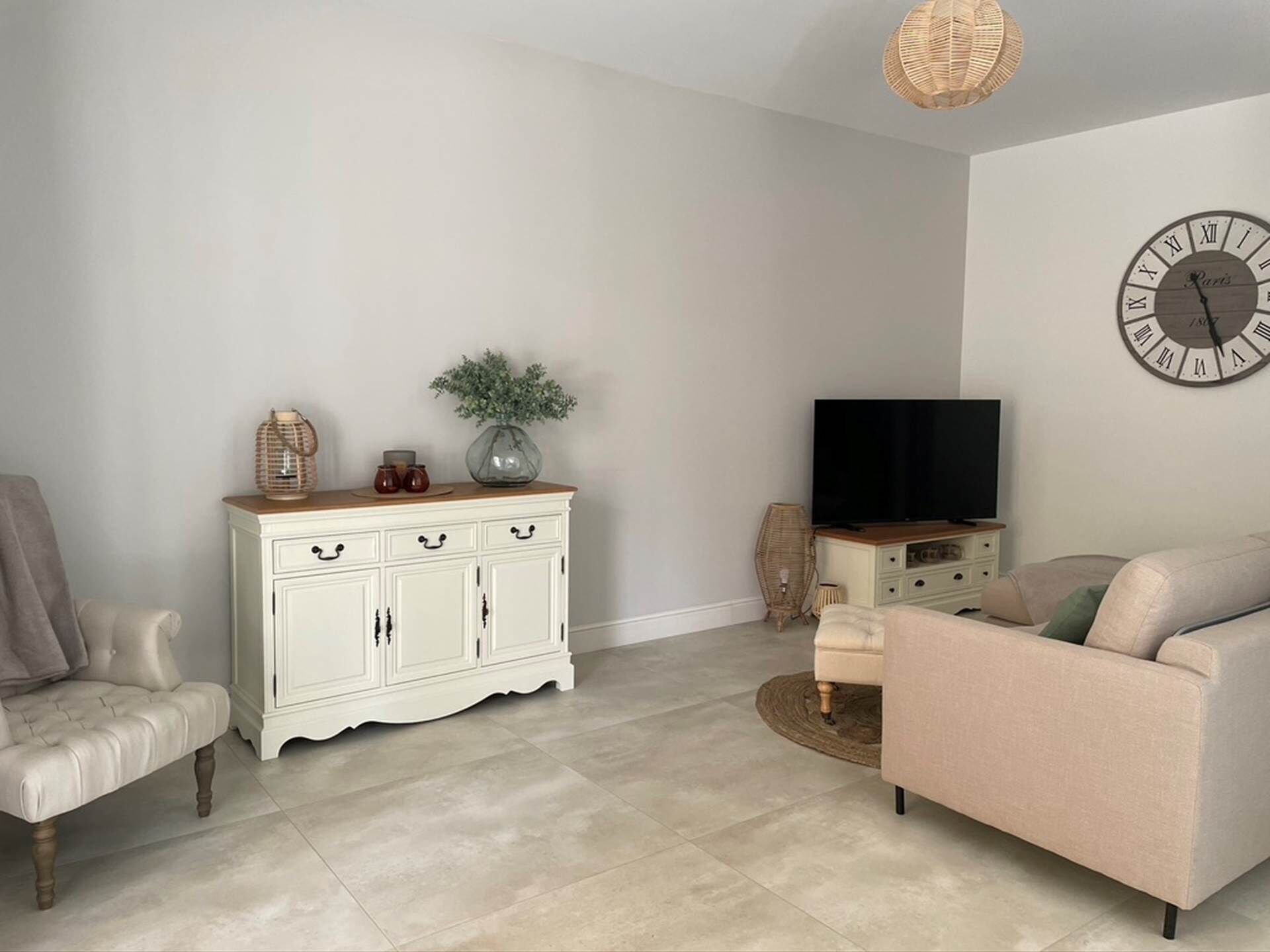 A living room with a white cabinet, a beige sofa, a television, and a wall clock.