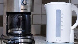 Une cafetière en acier inoxydable dotée d’un écran numérique et une bouilloire électrique blanche, posées sur un plan de travail de cuisine.
