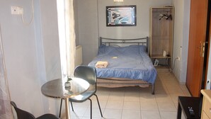 Une petite pièce, bien rangée, avec un lit simple, une chaise, une table et une armoire.